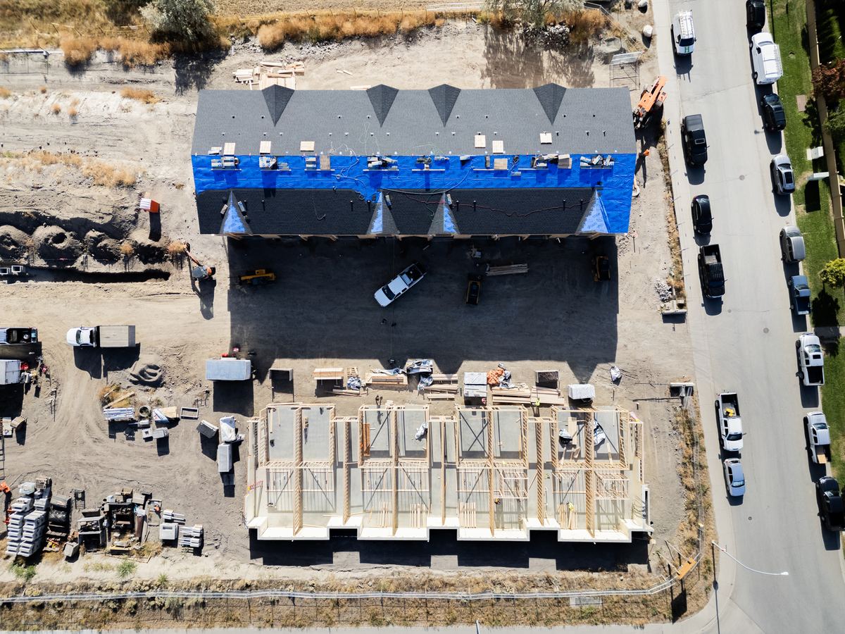 Aerial view of roofing going on the first building while the second is framed