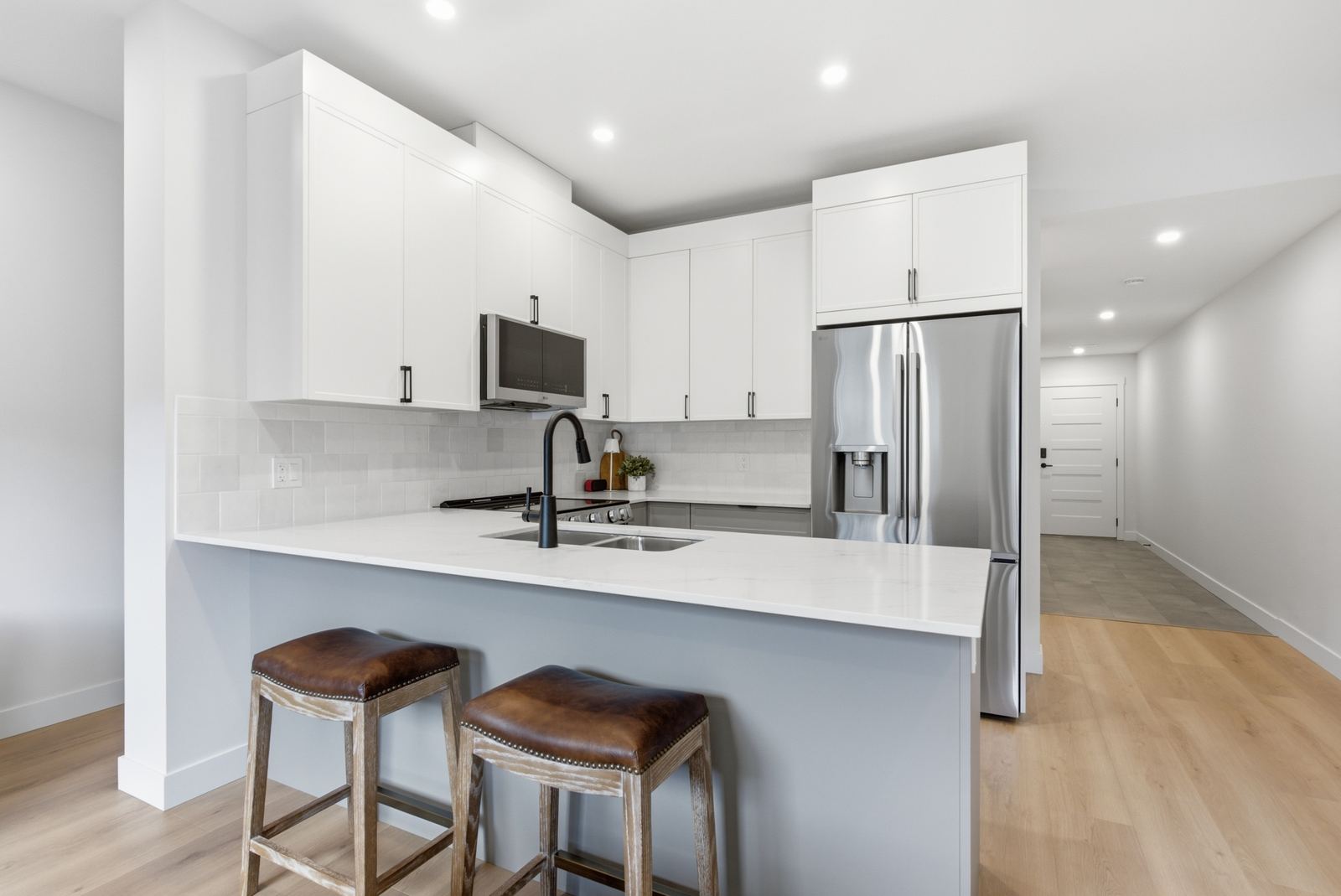 Show home kitchen with white shaker cabinets, quartz island with two stools and stainless appliances