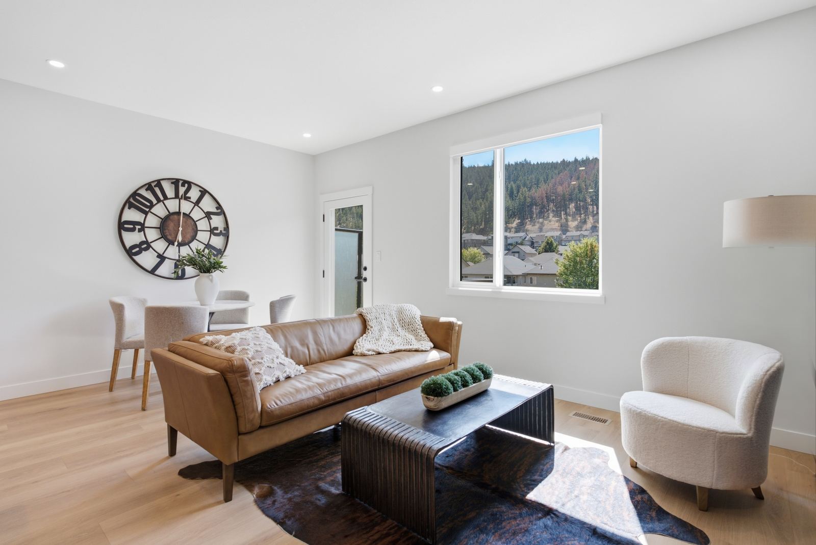 Show home living room with leather sofa, light wide-plank floors and a window to the hillside